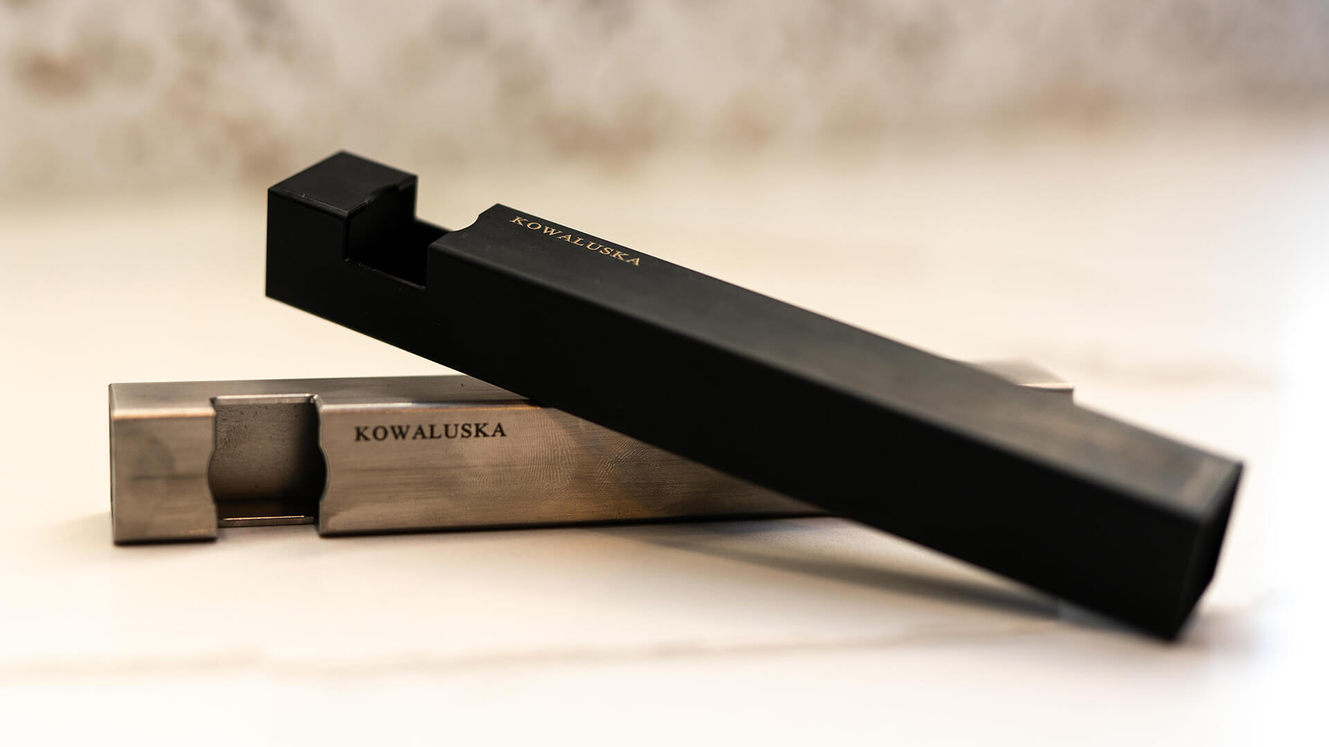 A pair of unique-bar-shaped bottle openers shown. One has the black oxide coating and the other one is shown in our aeroapace grade 300 series stainless steel